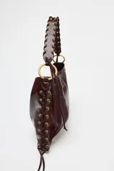 Bolso de hombro marrón oscuro con acabado brillante, asa trenzada y ojales metálicos en los laterales.