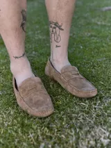 Mocasín de cuero gamuzado color marrón claro, con punta redonda y detalle de costuras a la vista.