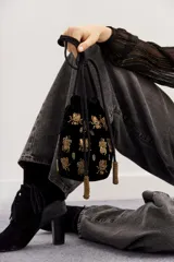 Cartera tipo bombonera negra de terciopelo con bordado de lentejuelas y canutillos dorados con forma de insectos. Tiene cordón de ajuste con borlas de canutillos dorados y correa de mano.