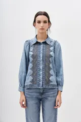 Camisa de denim celeste con bordados geométricos en el frente, corte recto, cuello camisero, manga larga con frunces en los hombros y puños abotonados.