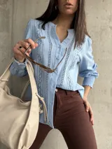 Camisa celeste de manga larga con cuello mao y cierre frontal con botones. Presenta detalles de broderie en el frente y mangas.