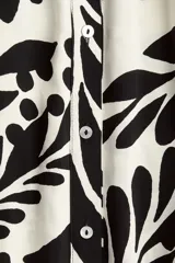 Vestido midi camisero con estampado floral en blanco y negro, cuello camisero, botonadura frontal y mangas cortas. Incluye cinturón extraíble para atar.