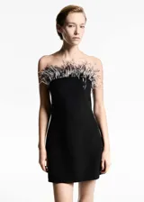 Vestido corto negro de fiesta con escote palabra de honor y adorno de plumas en el borde superior.