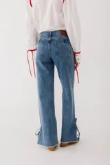 Pantalón de jean azul oscuro de corte recto, con cintura alta con cinturón del mismo material y detalle de flecos en la cintura y en los tobillos.