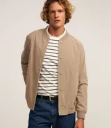 Campera bomber color beige de pana, con cuello redondo, cierre con botones a presión, bolsillos laterales y puños y cintura elastizados.