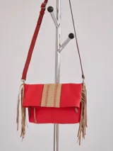 Bandolera roja con solapa y flecos de cuero color beige. Presenta una franja central tejida en tonos beige y blanco. El asa es de cuero rojo y es regulable.
