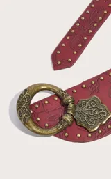 Cinturón ancho de cuero color rojo con diseño floral repujado, tachas doradas y hebilla circular de metal envejecido.
