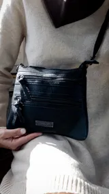 Bandolera negra con correa larga regulable y múltiples bolsillos frontales con cierre.