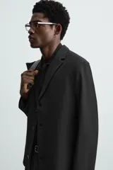 Blazer negro de corte regular, con cuello de solapas de muesca, manga larga con puños abotonados, bolsillos laterales ocultos en la costura de la cadera, bolsillo interior y cierre frontal con botonadura.