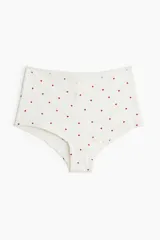 Bombacha shortie de tiro alto en punto pointelle de algodón color blanco con estampado de corazones rojos. Presenta ribete de encaje en la cintura y tapeta de botones decorativa.
