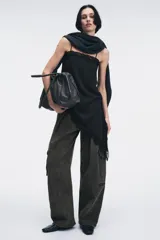 Top negro con estampado de lunares blancos, escote recto, tirantes finos, detalle de encaje en el escote y bajo asimétrico con abertura lateral.