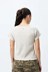 Remera color beige de punto acanalado con silueta relajada y manga corta raglán. El detalle de ruedo con terminación ondulada le aporta un aire fresco y juvenil.