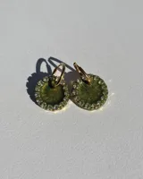 Par de aros colgantes con forma circular, de resina color verde musgo con glitter y borde de strass. El aro es de acero quirúrgico dorado.