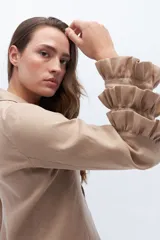 Blazer color beige confeccionado en lino, con cuello solapa, cierre frontal con un botón y mangas largas con volantes en capas.