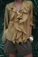 Camisa color verde oliva de tela traslúcida con escote en V, mangas largas abullonadas con puños elásticos y volantes en el frente.