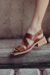 Sandalias de cuero color marrón con tiras cruzadas, taco de 4cm y cierre con hebilla metálica ajustable en el tobillo.