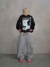 Pantalón deportivo gris de corte ancho y holgado, con cordón de ajuste en la cintura y un estampado de camuflaje sutil en la parte superior, visible bajo la campera.