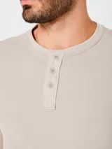 Camiseta beige de manga larga con cuello redondo y tapeta con botones. Tejido texturizado tipo waffle.
