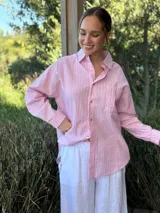 Camisa holgada a rayas verticales color beige y blanco, con cuello clásico, manga larga, bolsillo en el pecho y cierre frontal con botones nacarados.