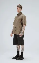 Camisa de manga corta color verde militar con cuello camisero y botones frontales oscuros. La tela presenta un patrón texturizado o estampado sutil en tono similar.