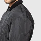 Chaqueta negra acolchada con diseño de rombos, cuello de pana y cierre frontal con botones a presión.