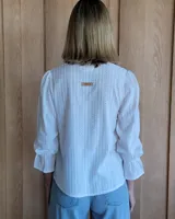 Blusa color beige con cuello con volados, mangas largas abullonadas con puños elásticos y cierre con botones en la parte delantera.