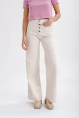 Pantalón de jean color beige, de corte palazzo, con bolsillos frontales con botón y bolsillos traseros.