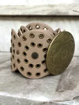 Cinto faja color beige con hebilla circular de metal dorado con diseño labrado.