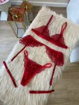 Conjunto de lencería rojo de encaje, compuesto por un bralette con breteles regulables, una tanga regulable con corte media less y un portaligas con volados.