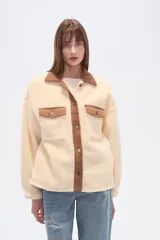 Campera estilo camisa (shacket) de tejido tipo borrego o sherpa color crema, con cuello y tapeta de pana marrón. Posee dos bolsillos frontales con tapa y botones a presión.