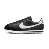 Zapatillas Nike Cortez negras con swoosh blanco de cuero, suela de goma blanca con línea negra y refuerzo blanco en el talón.