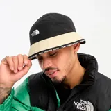 Gorro tipo pescador negro con banda color crema y logo de The North Face bordado en blanco.