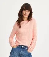 Sweater de punto color rosado pálido, con textura ondulada y pequeños orificios en el tejido. Presenta cuello redondo y mangas largas con puños acanalados.