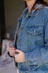 Campera de jean celeste con capucha gris de algodón desmontable, cierre con botones metálicos y bolsillos delanteros.