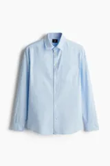 Camisa celeste de lino y algodón, corte regular, manga larga, cuello inglés, bolsillo en el pecho y cierre con botones.