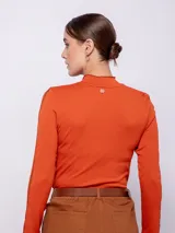 Top de manga larga color naranja con cuello alto, confeccionado en tela de textura diferenciada y detalles de costura en los puños.