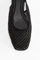 Sandalias bajas negras con capellada de malla tejida, punta fina y tira trasera con hebilla dorada.