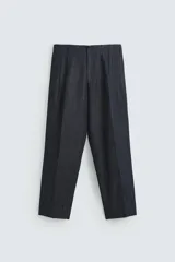 Pantalón de denim azul oscuro, corte wide fit, largo cropped, con pliegues frontales, bolsillos laterales y traseros asimétricos. Cierre frontal con cremallera y gancho metálico oculto.