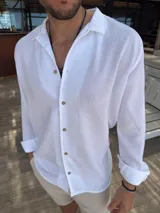 Camisa blanca de fibrana con cuello clásico, manga larga con puños arremangados y cierre frontal con botones de madera.