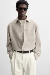 Camisa color crema de corte relaxed fit, confeccionada en tejido de mezcla de algodón suave al tacto. Tiene cuello solapa, manga larga con puños abotonados, un bolsillo de parche en el pecho y cierre frontal con botones.