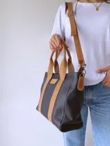 Cartera negra de cuero con forro de tela, doble asa corta color camel y correa larga desmontable también color camel.