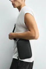 Bandolera negra con textura grabada, compartimento principal con cierre de cremallera, bolsillo interior plano, bolsillo frontal plano y asa de hombro ajustable y extraíble.