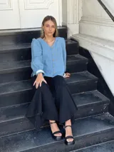 Camisa celeste de jean con cuello en V, mangas largas abullonadas con puños de encaje y cierre frontal con botones.
