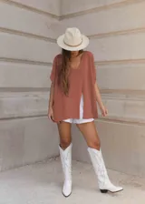 Poncho escotado color ladrillo, de tejido de punto con hilado italiano. Presenta tajos laterales y tajo frontal.