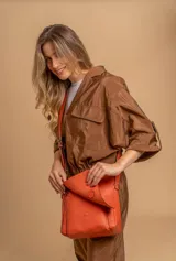 Bandolera de hombro color gris claro, con solapa frontal y correa ajustable. Presenta un diseño simple y práctico, ideal para uso diario.