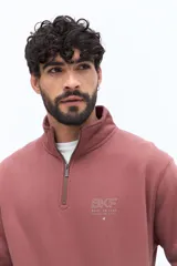 Buzo de algodón gris oscuro con cuello alto y cierre frontal parcial. Presenta un parche de marca en la manga izquierda y un logo bordado en el pecho.