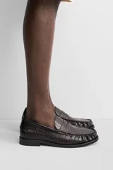 Mocasín de vestir color marrón oscuro con grabado tipo cocodrilo, horma redonda y suela con ligero tacón.