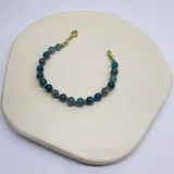 Pulsera elástica con cuentas de apatita azul verdoso de 6mm, separadores de hilo turquesa y terminaciones de acero hipoalergénico con baño dorado.