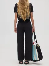 Pantalón negro de algodón, corte holgado y pierna ancha con pretina elástica. Presenta rayas blancas y celestes a los costados.