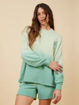 Sweater color crema con degradé a naranja, con cuello redondo y logo estampado de palmera en el pecho.